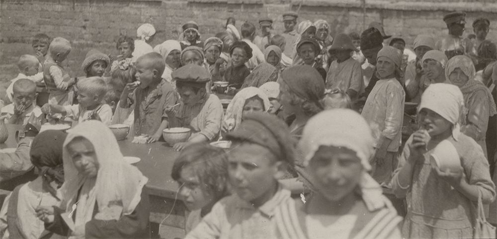 Black and white photograph of children eating at an outdoor ARA kitchen in Odessa, Ukraine, circa 1922.