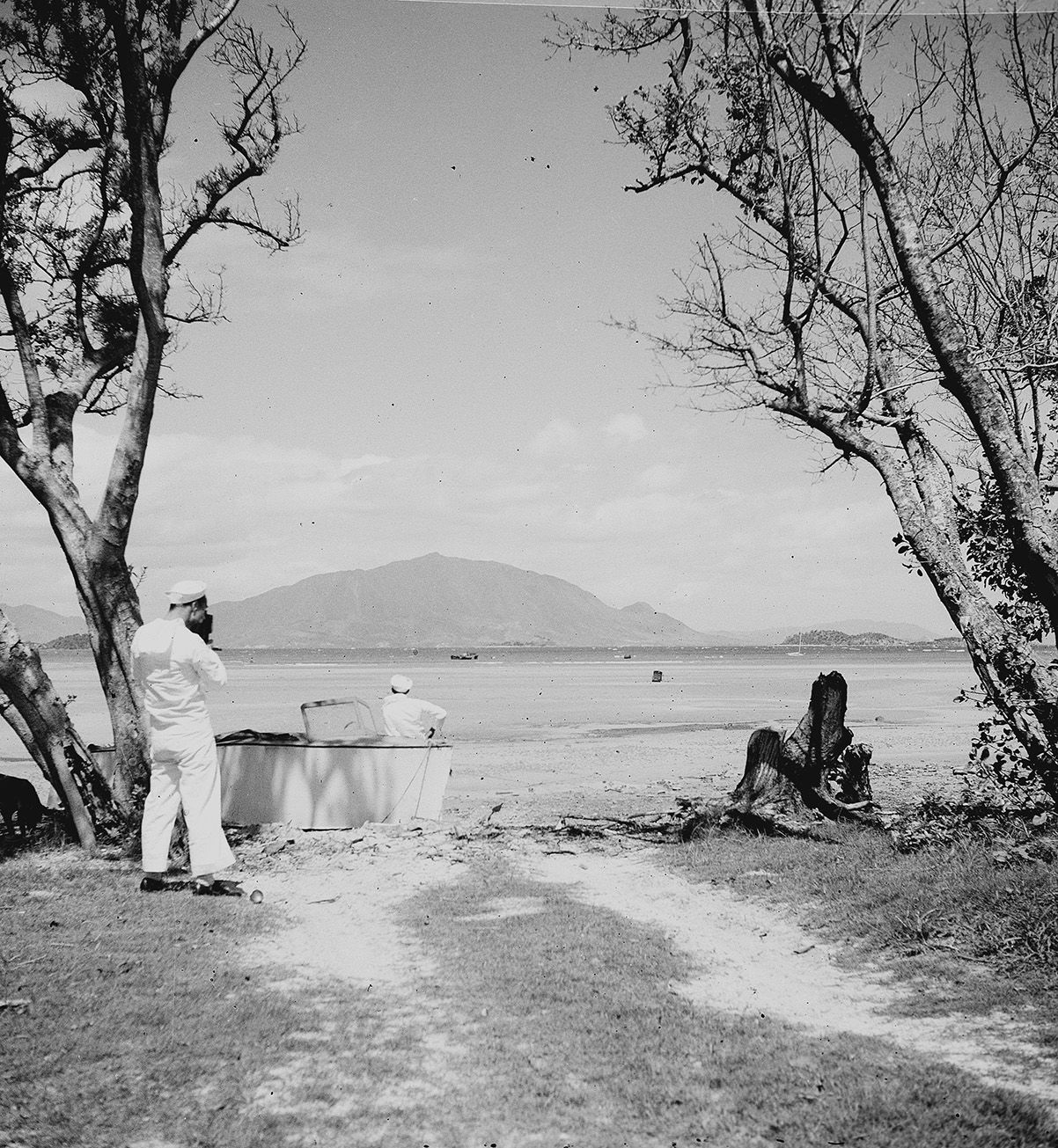 Black and white photograph showing Ed Keegan from behind photographing a Seabee looking across Magenta Bay to Mont Dore, New Caledonia, 1943–1945.