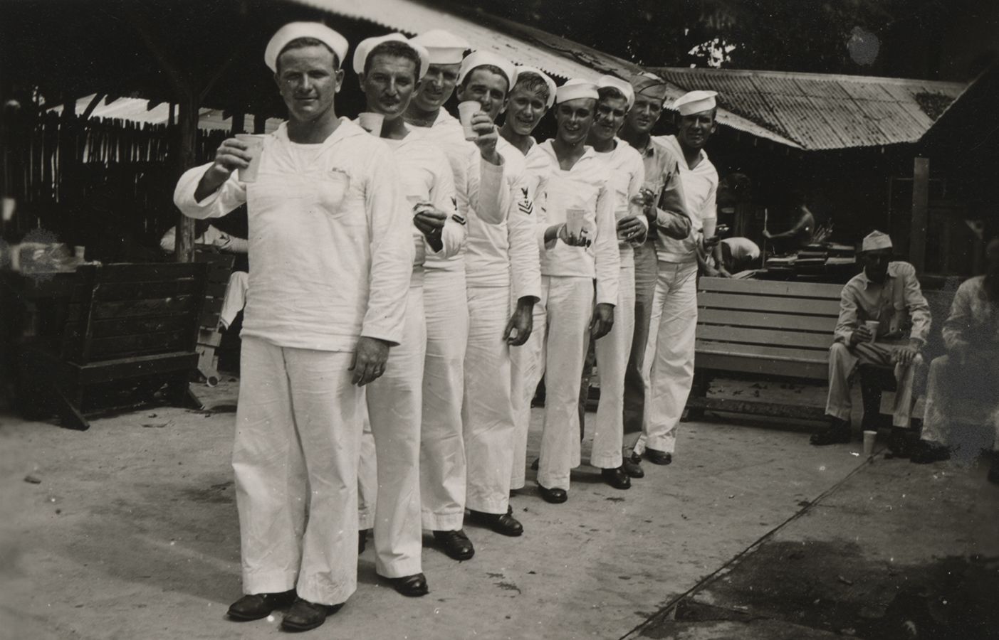 Black and white photograph of nine Seabees lined up for a toast, New Caledonia, 1944–1945.