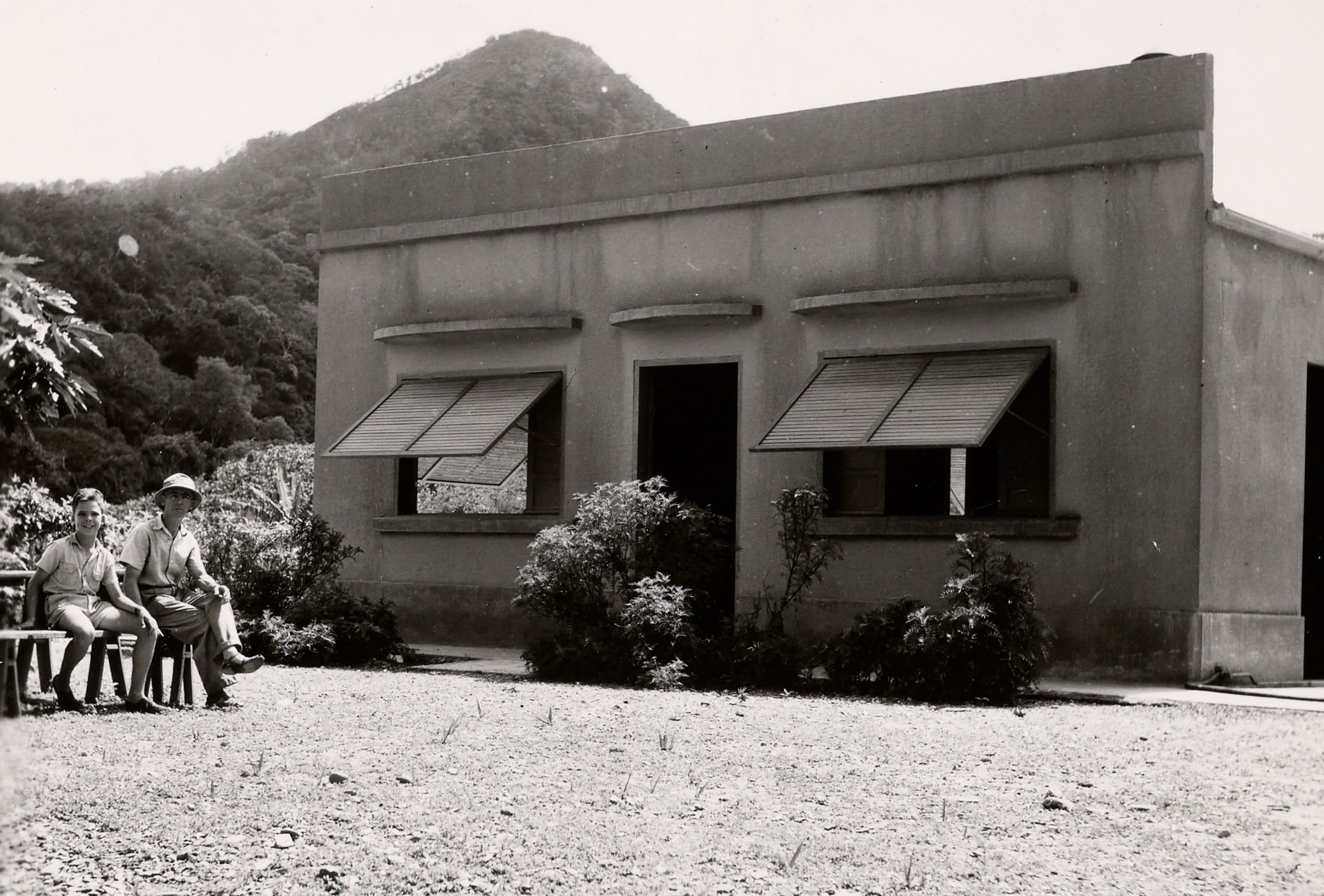 Black and white photograph of two Caldoches people seated in front of their summer home towards the north of New Caledonia, 1944.