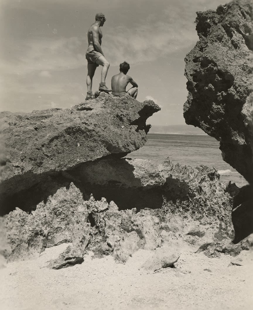 Black and white photograph of Frank Denny (standing) and Nat Bellantoni (seated) on a craggy rock on the shore of Okinawa, 1945.